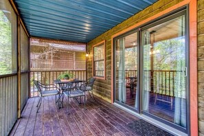 A covered porch with a table and chairs, large glass doors, and a view of trees. - Foxes Den (Pigeon Forge)