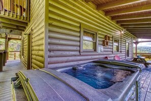 Een vakantiehuisje van hout met een jacuzzi en een terras.