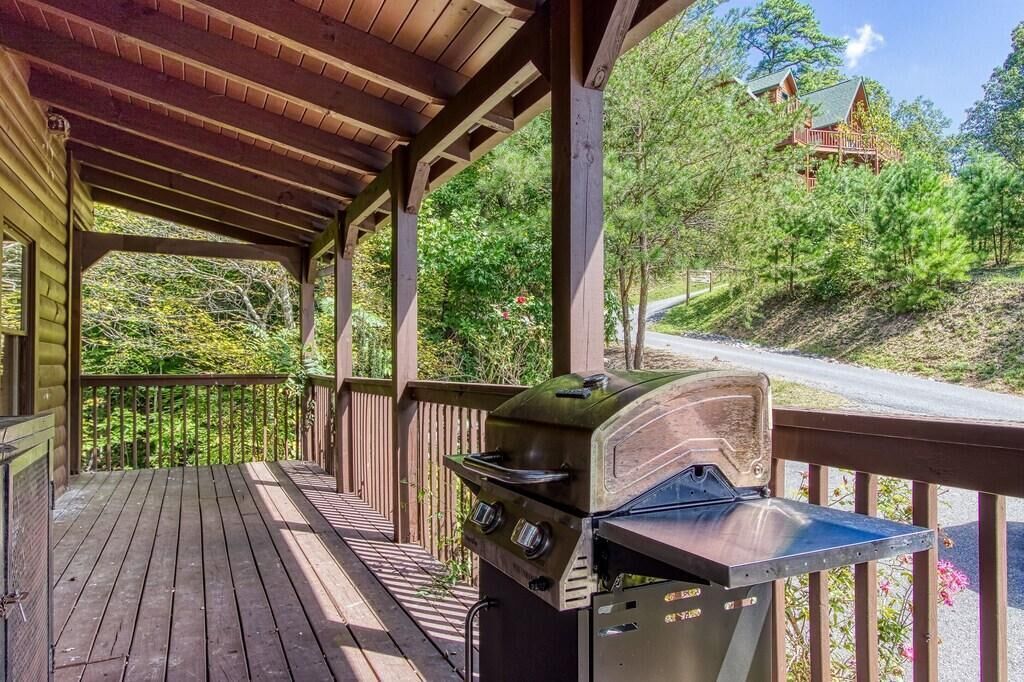 A covered outdoor area with a grill, wooden deck, and a view of a house on a hill.