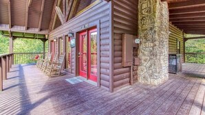 A log cabin with a porch, a stone chimney, and a red door. - Goldilock's Cottage (Sevierville)