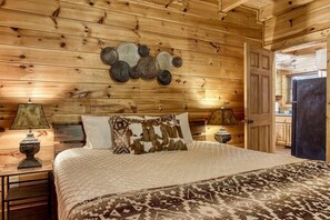 Een slaapkamer in chaletstijl met een bed, kussens, een nachtkastje, een lamp en een decoratie aan de muur.