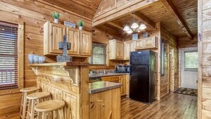 A wooden cabin interior with a kitchen area, bar stools, and a refrigerator. - Goldilock's Cottage (Sevierville)