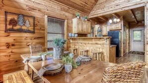 A wooden cabin interior with a dining table set, wooden cabinets, and a kitchen area. - Goldilock's Cottage (Sevierville)
