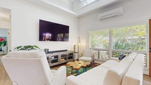 Una sala de estar moderna con un sofá, sillas, una mesa de centro, un televisor y un ventanal con persianas.
