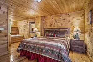 Ein Schlafzimmer in einer Holzhütte mit einem Bett, einem Nachttisch und einem kleinen Schreibtisch mit einer Lampe.
