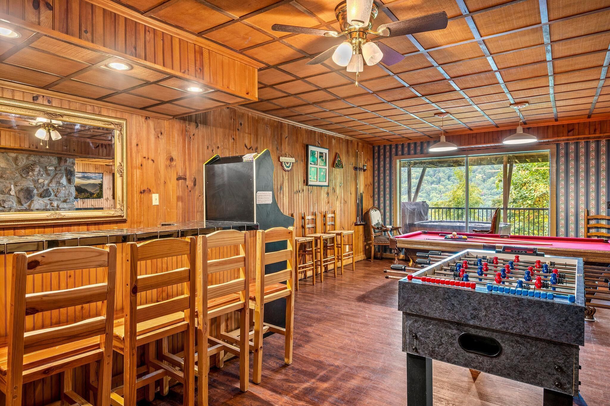 A wooden-floored room with a foosball table, pool table, and seating area.