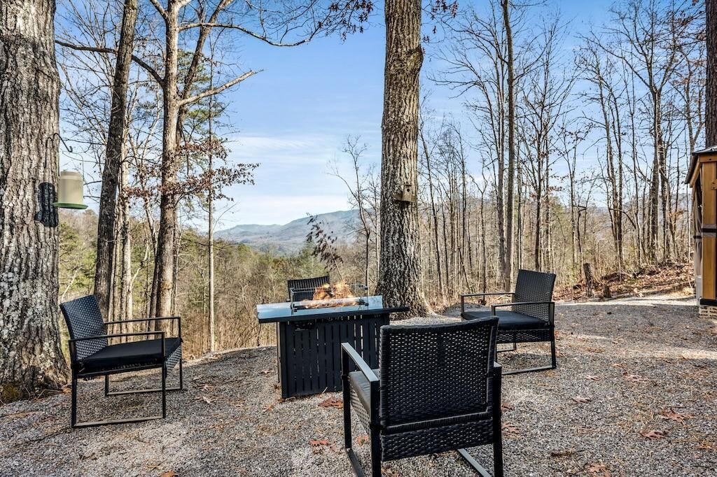 An outdoor seating area with chairs and a grill, surrounded by trees and a view of the mountains.