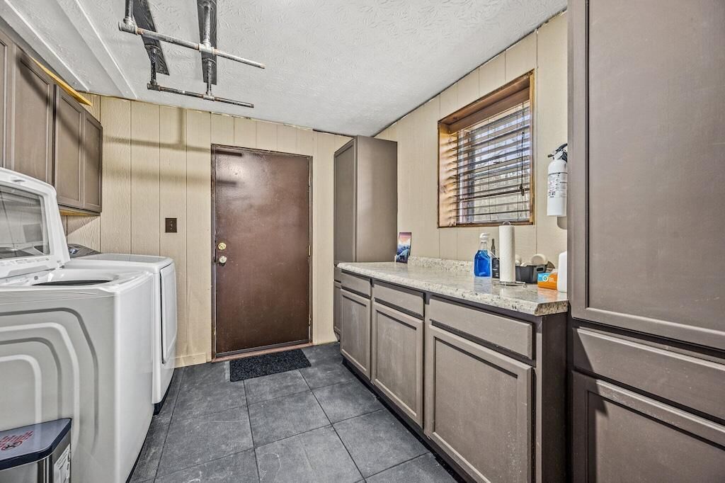 A compact kitchen with a washing machine, a refrigerator, and a window with blinds.
