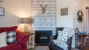 Una sala acogedora con chimenea, un sofá rojo, un sillón de cuero marrón y una decoración de cabeza de venado montada en la pared.