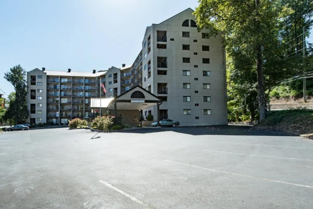 Un hotel a più piani con un ingresso centrale, un parcheggio e una bandiera.