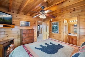 Ein Holzblockhaus-Innenraum mit Bett, Kommode, Fernseher, Deckenventilator und gerahmten Bildern.