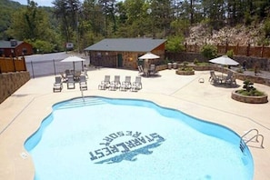 Ein Schwimmbecken mit Liegestühlen und Sonnenschirmen, umgeben von einem Steinhaus und Bäumen.