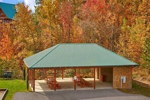 Ein überdachter Pavillon mit Tischen und Bänken, umgeben von Bäumen mit Herbstlaub.
