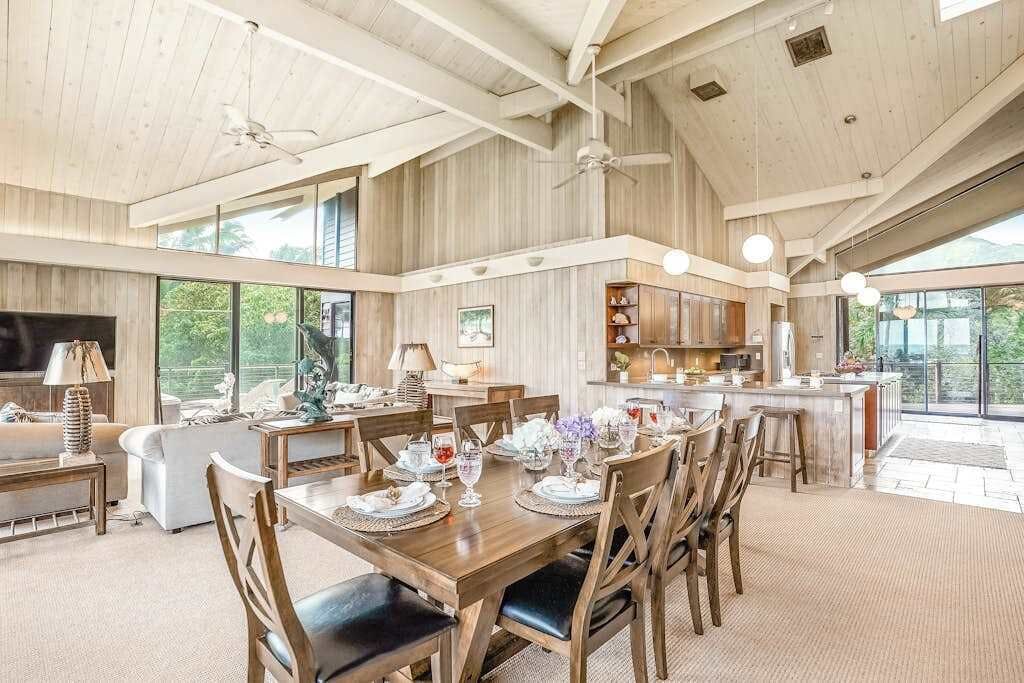 A spacious dining area with a high ceiling, wooden beams, and large windows offering views of the outdoors.