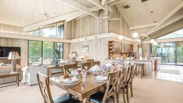 A spacious dining area with a high ceiling, wooden beams, and large windows offering views of the outdoors.