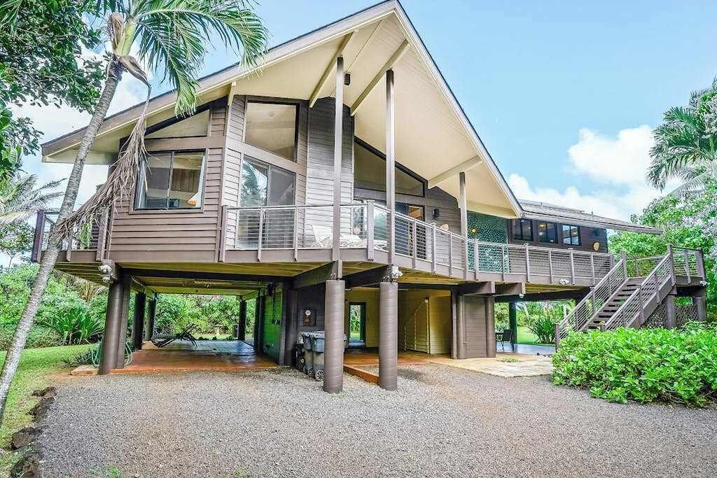 A two-story house with a covered outdoor area, a staircase, and a view of the surrounding greenery.
