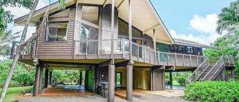 A two-story house with a covered outdoor area, a staircase, and a view of the surrounding greenery.