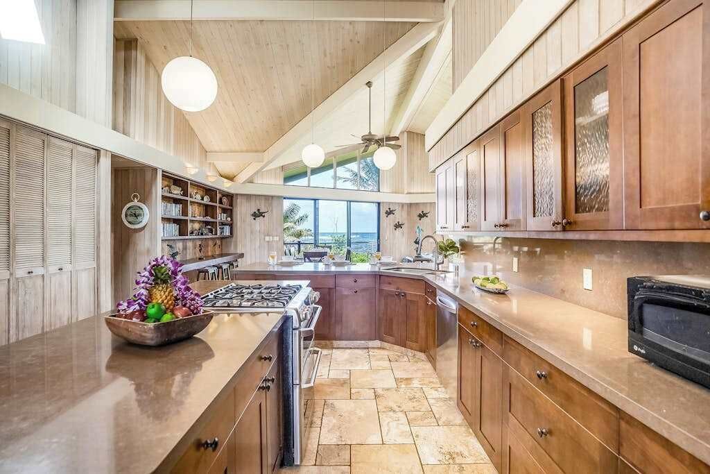 A kitchen with a central island, wooden cabinets, a stove, and a view of the outdoors.