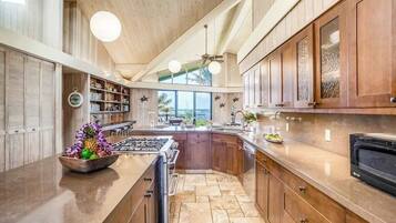 A kitchen with a central island, wooden cabinets, a stove, and a view of the outdoors.