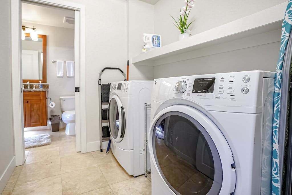 A laundry room with two front-loading washing machines, a dryer, and a shelf above the machines.