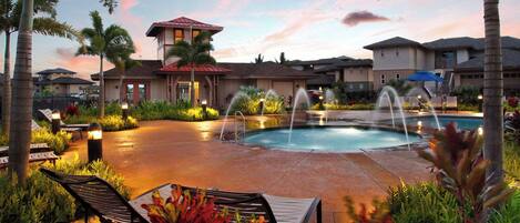 A pool area with a fountain, lounge chairs, and a building with a red roof.