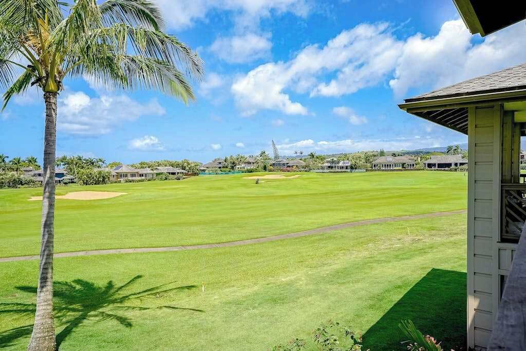 Um campo de golfe com vista clara para o green, uma palmeira e um edifício com telhado inclinado.