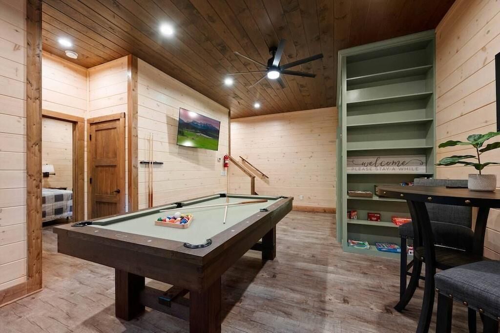 A pool table with cue sticks, a television mounted on the wall, and a 'welcome' sign on a shelf.