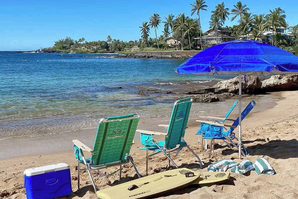 A beach with chairs, a cooler, and a surfboard.