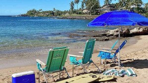 Una playa con sillas, un enfriador y una tabla de surf.