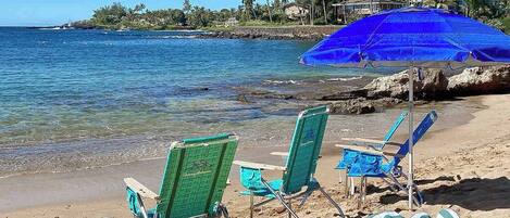 A beach with chairs, a cooler, and a surfboard.