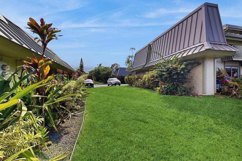 A residential area with a well-maintained lawn, parked cars, and houses with sloped roofs.