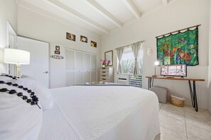 Ein Schlafzimmer mit einem Bett, einem Nachttisch mit Lampe, einem Fenster mit Vorhängen, einem an der Wand montierten Fernseher und einer Tür mit dem Schild 'Gone to Board Meeting'.