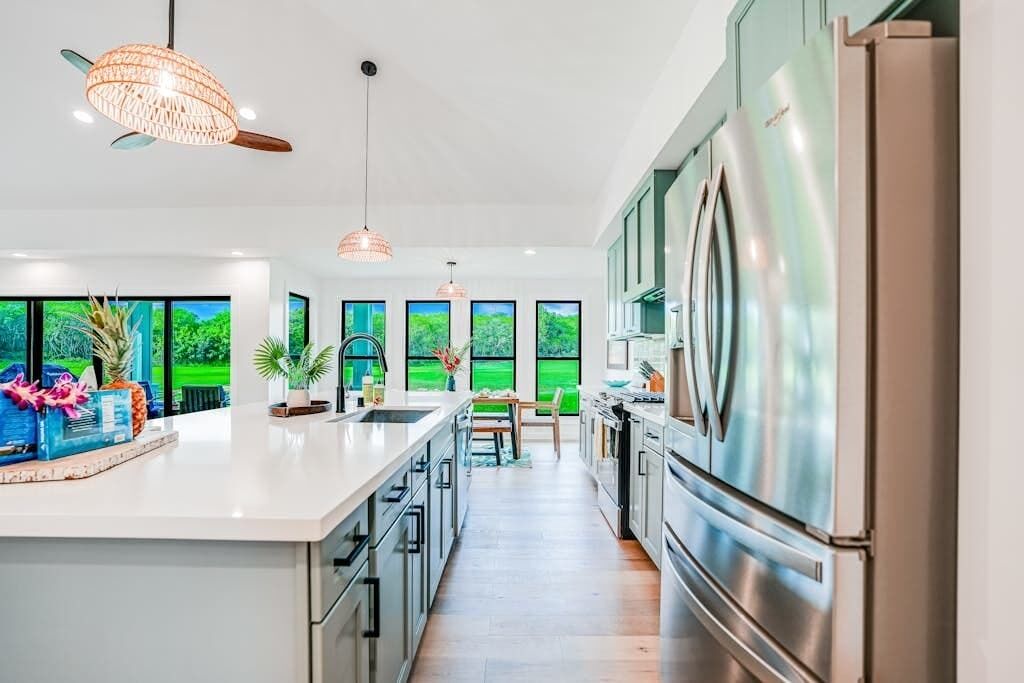 Een moderne keuken met een groot kookeiland, roestvrijstalen apparatuur en grote ramen met uitzicht op groen.