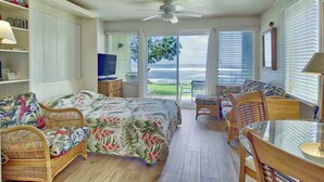 Slaapkamer met een bed, een televisie, een eettafel, stoelen, een plafondventilator en uitzicht op zee.