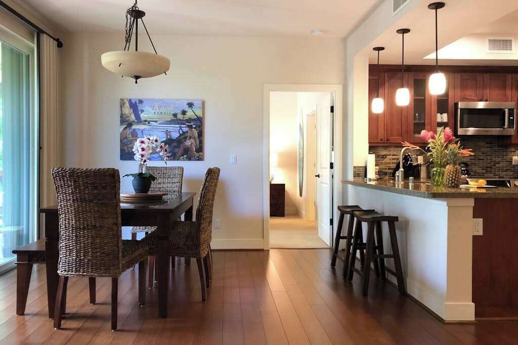 Una cocina moderna con una isla central, taburetes de bar y un comedor con sillas de mimbre.