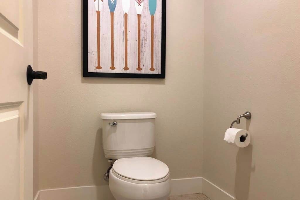 Un baño pequeño con un inodoro, una obra de arte enmarcada encima y un dispensador de papel higiénico en la pared.