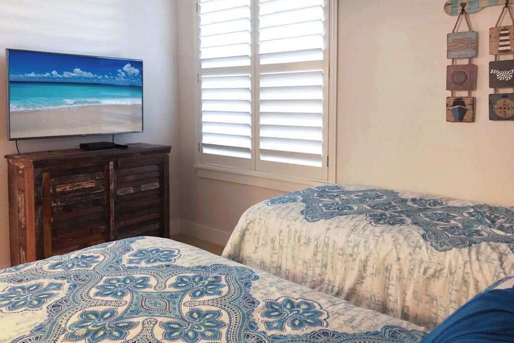 A bedroom with a TV, a window with blinds, and a bed with patterned bedding.