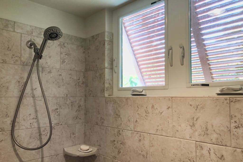 A bathroom with a shower, toilet, and a window with blinds.