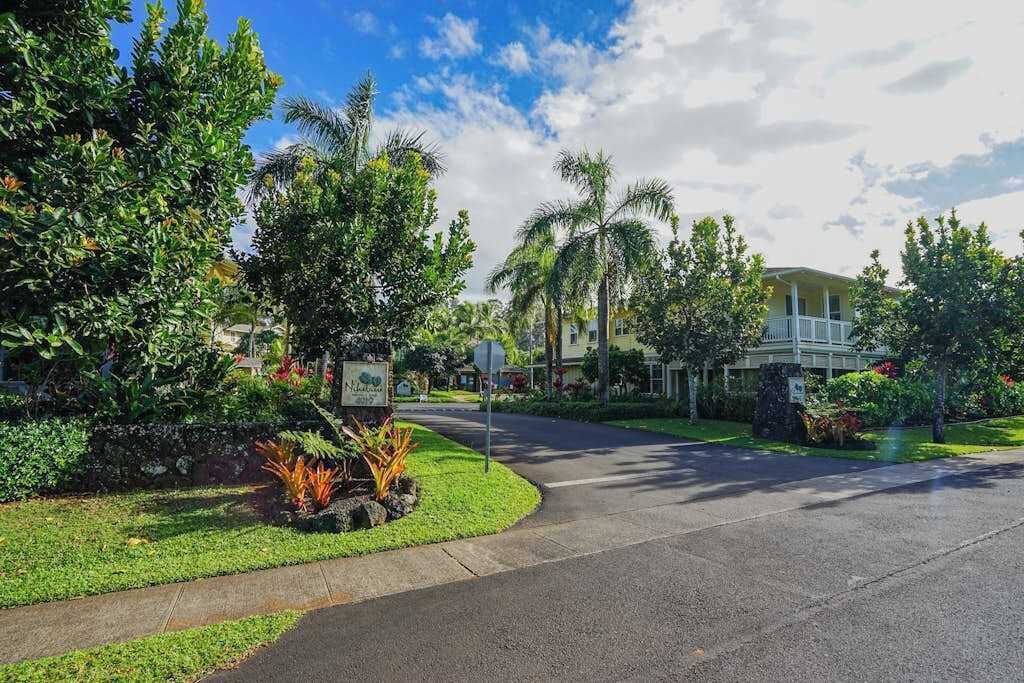 Una calle residencial con césped cuidado, palmeras y una casa con porche.