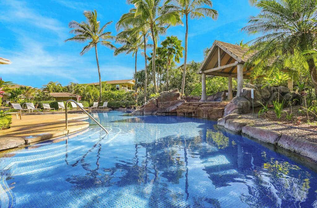Une piscine avec des chaises longues, des palmiers et un kiosque.
