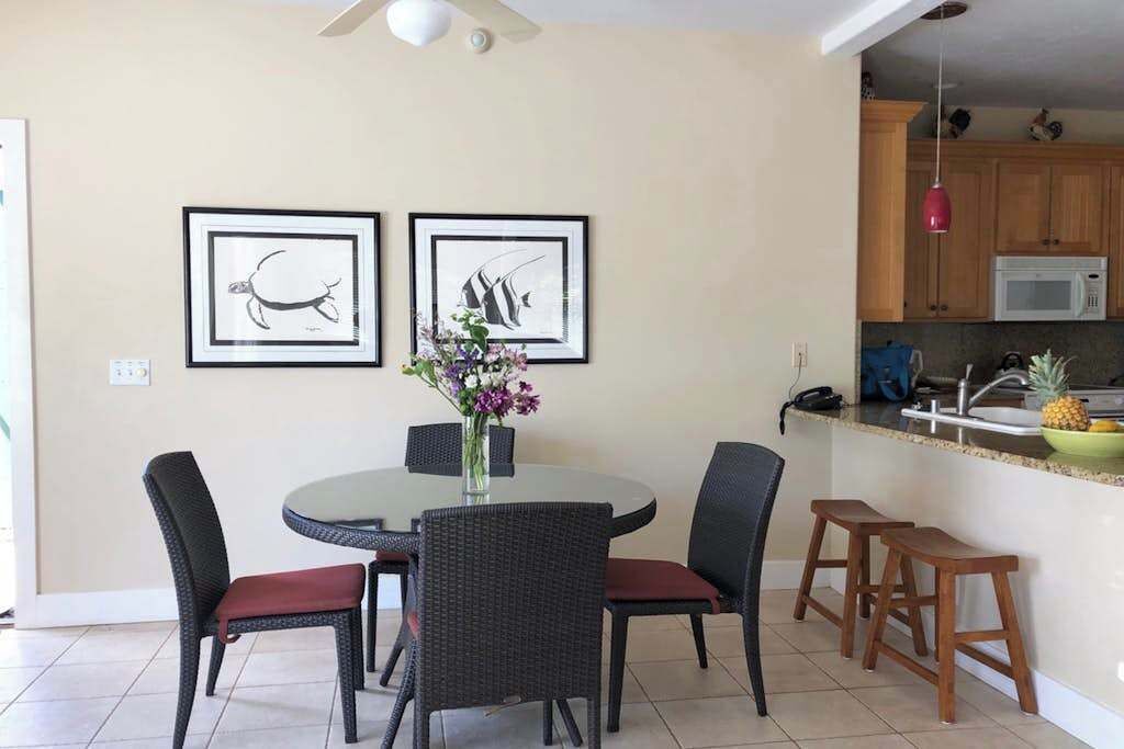 Comedor con una mesa redonda, cuatro sillas, un florero con flores y dos cuadros en la pared.