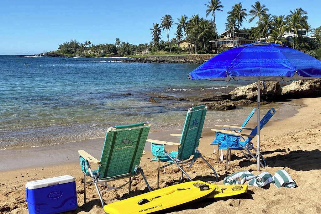A beach with chairs, a cooler, and a surfboard.