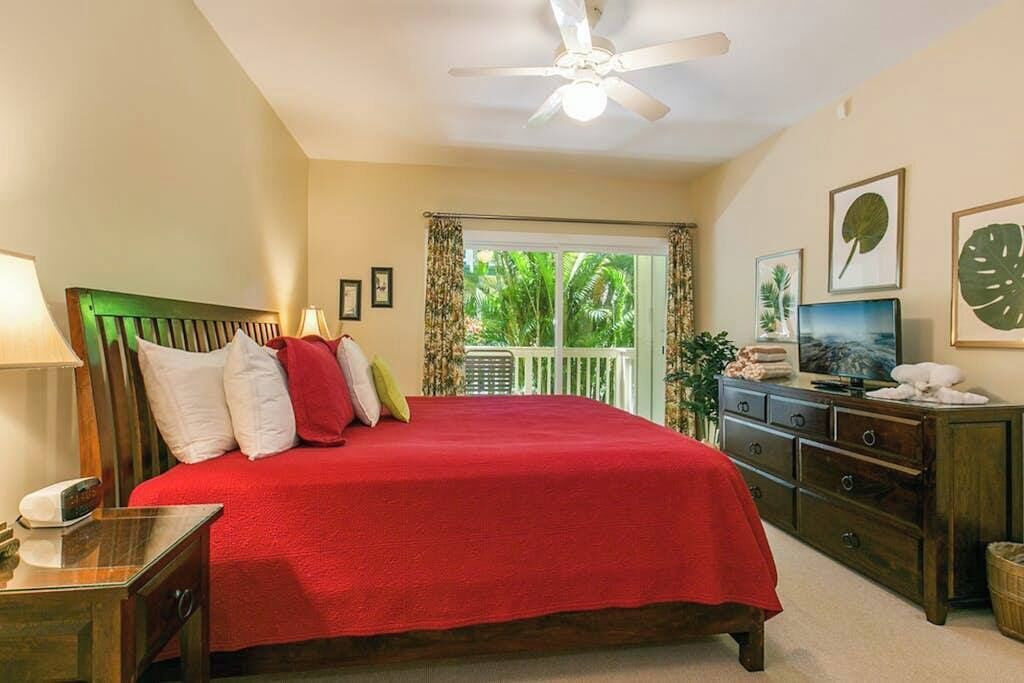 A bedroom with a bed, a ceiling fan, a TV, and a window with curtains.