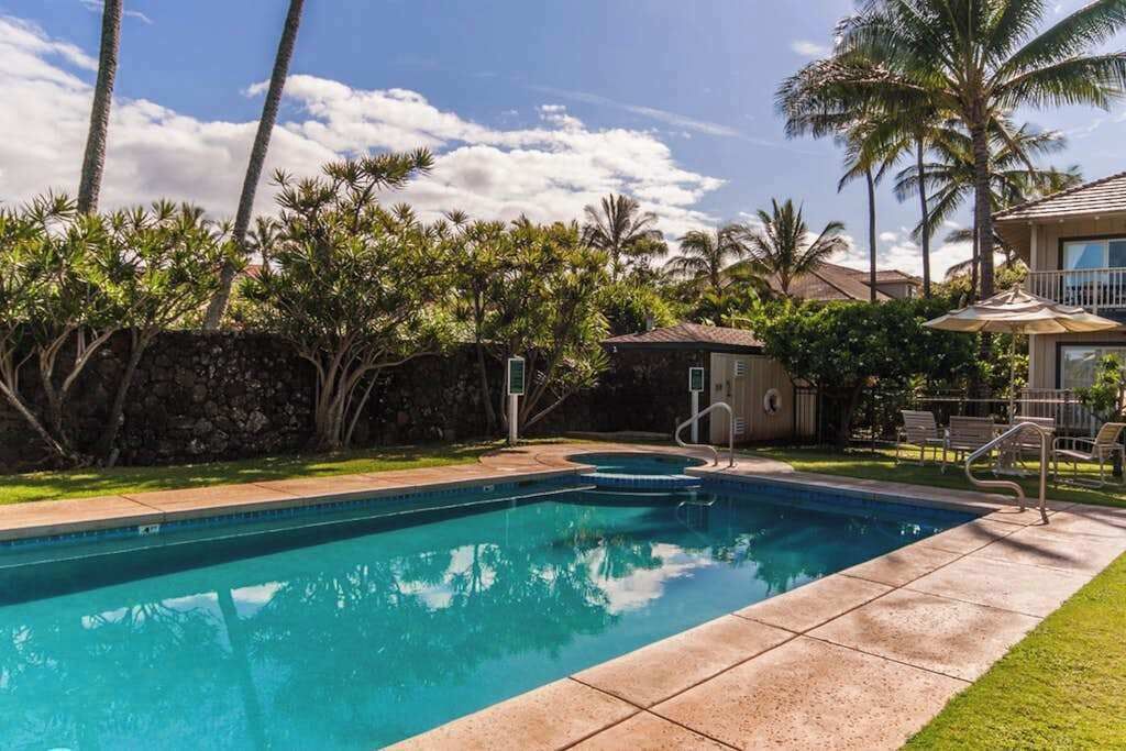 A swimming pool with a stone wall, palm trees, and a building with a balcony.