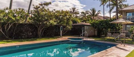 A swimming pool with a stone wall, palm trees, and a building with a balcony.