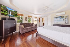 Ein Schlafzimmer mit einem großen Bett, einer Couch, einem Fernseher und einem Deckenventilator.