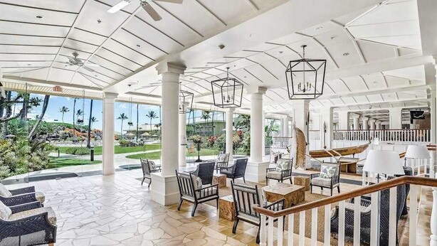 Un'ampia area interna con soffitto alto, ampie finestre e vista su un giardino curato.