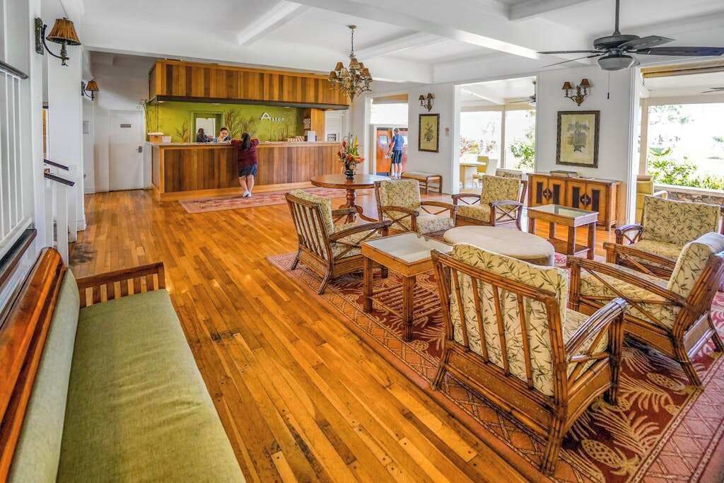 A spacious lobby with wooden flooring, a reception desk, and a seating area with patterned chairs and a sofa.