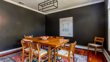 Une salle à manger avec une table et des chaises en bois, un tapis à motifs et un mur noir orné d’une affiche.