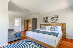 A bedroom with a bed, a grey sofa, a wooden wardrobe, and two abstract paintings on the wall.